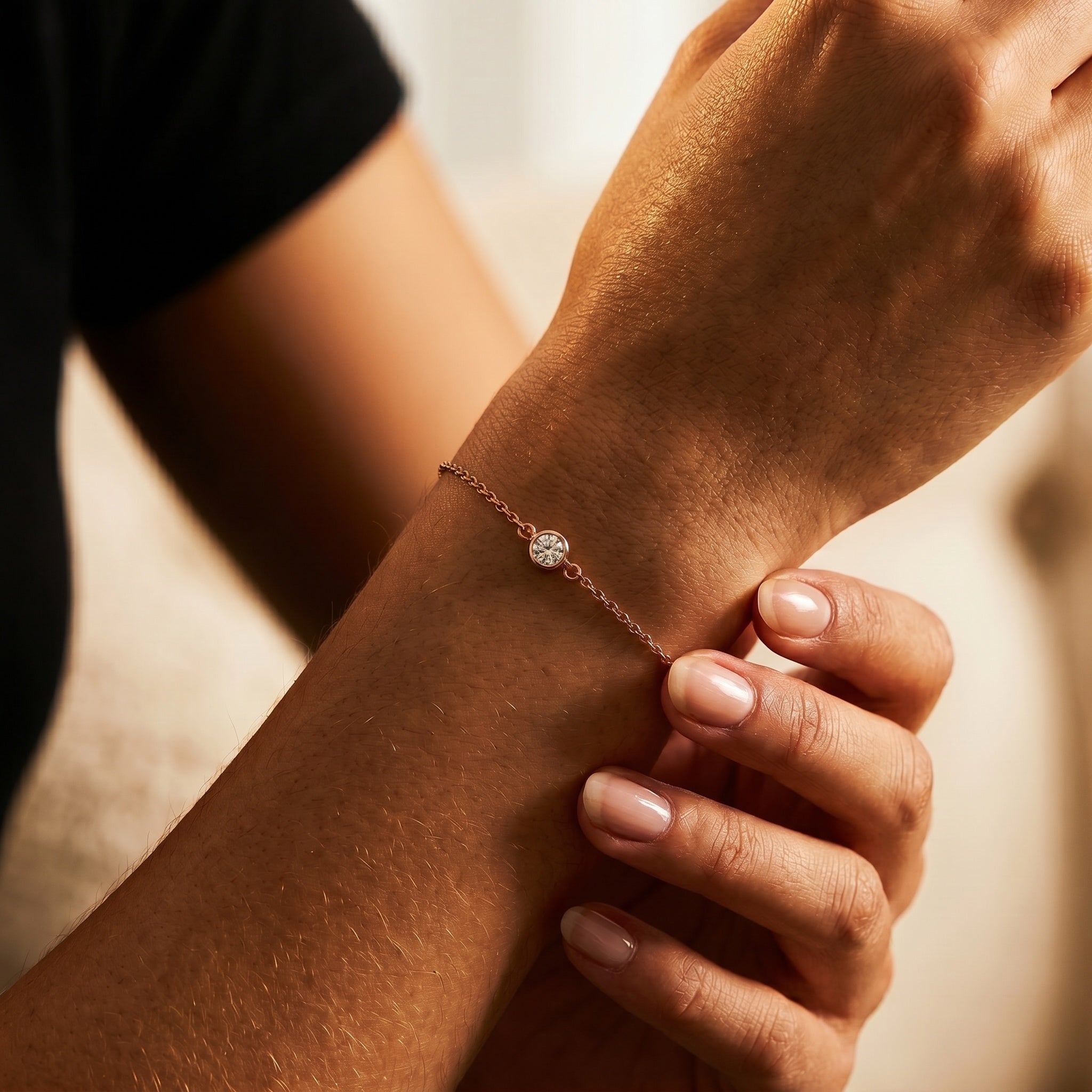 A delicate rose gold chain bracelet with a small round clear gemstone, shown being worn on a person's wrist with their other hand resting gently on top.
