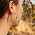 Close-up of a person wearing gold hoop earrings with a blurred natural background