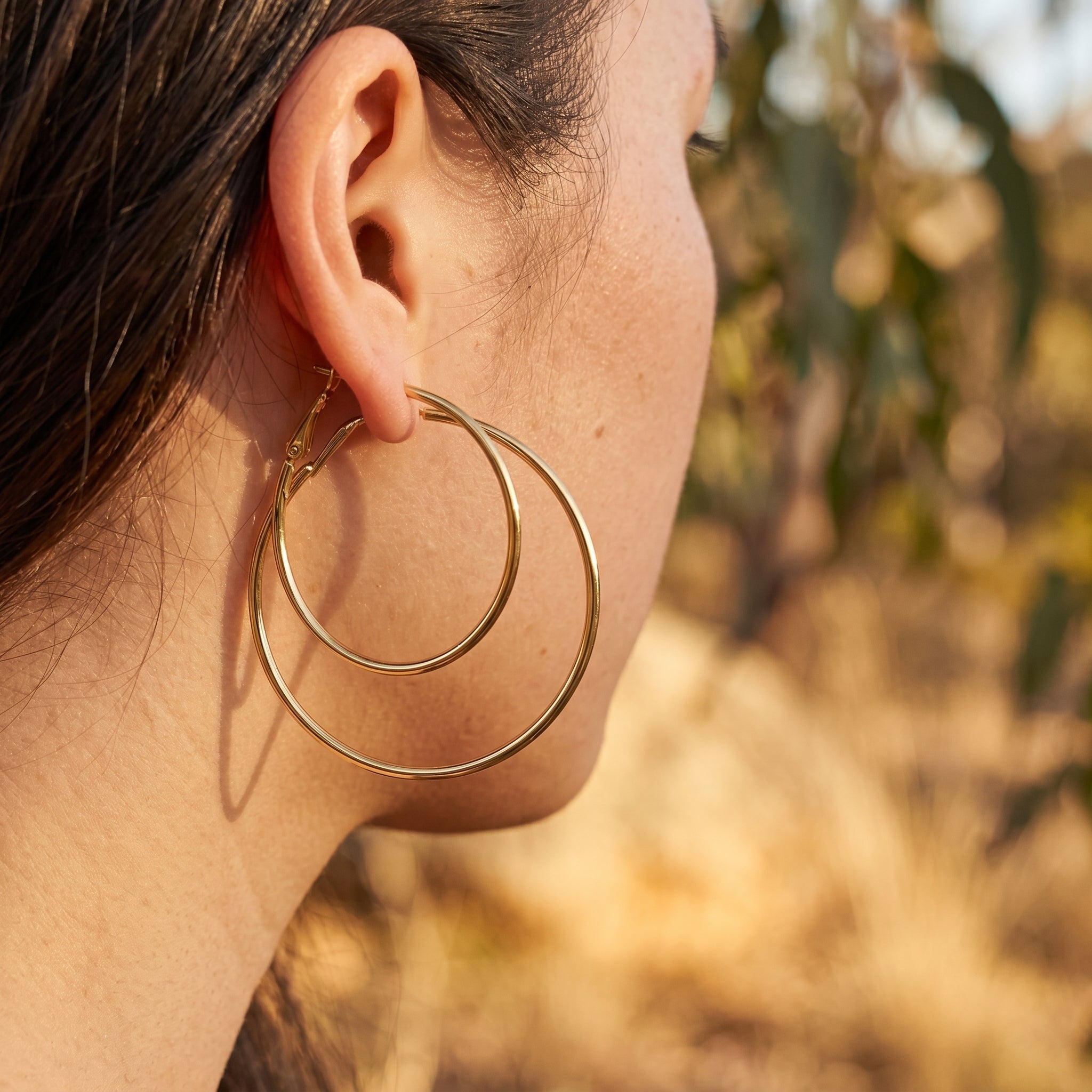 Close-up of a person wearing gold hoop earrings with a blurred natural background