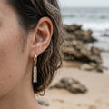 Close-up of an ear with a gold earring on a beach background