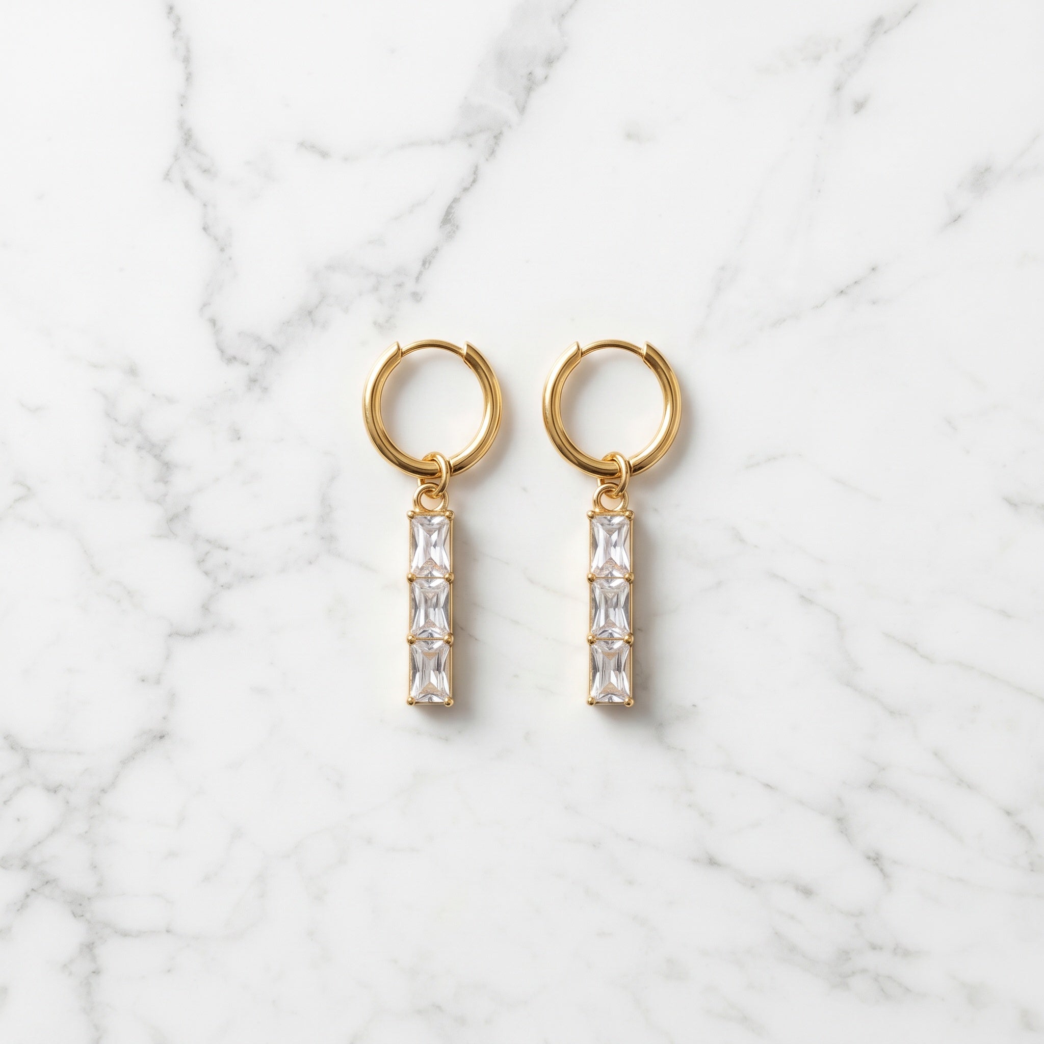 Gold hoop earrings with clear gemstones on a marble background