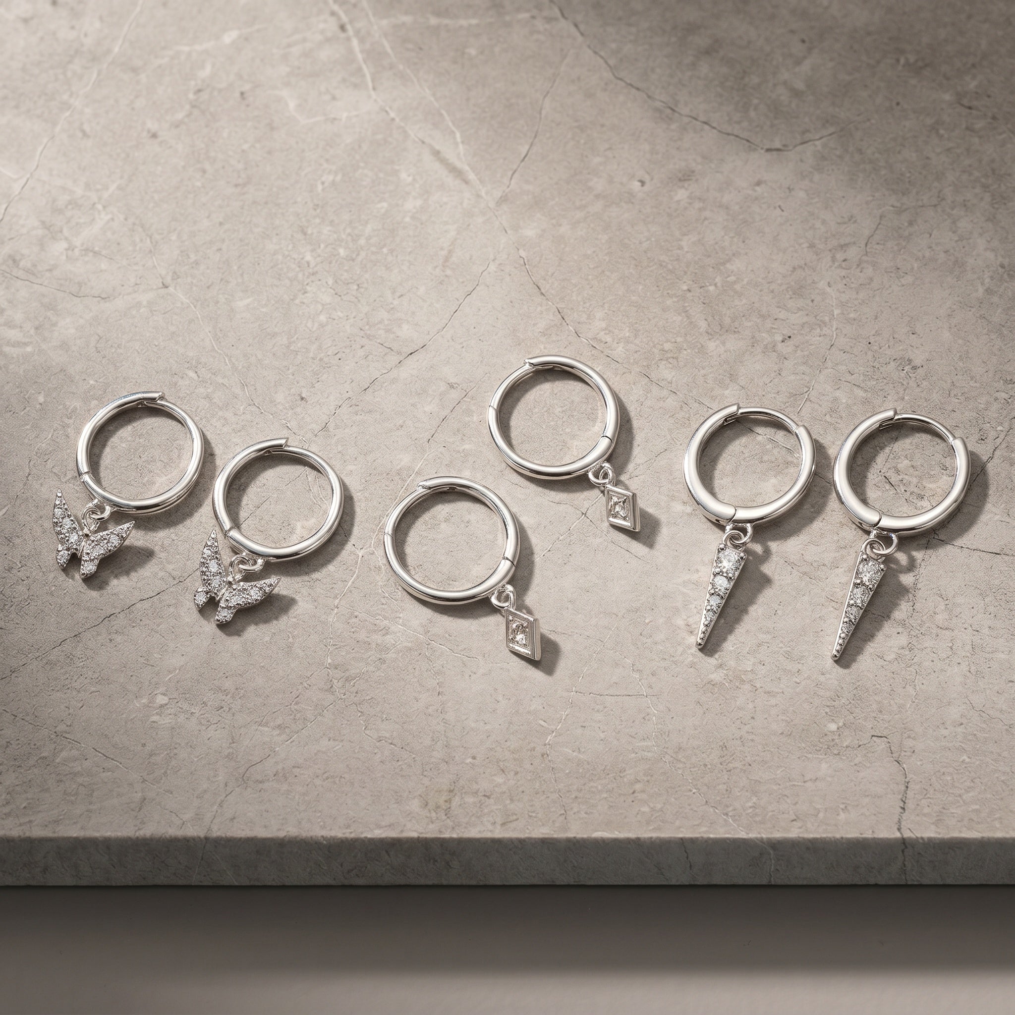 3 Pairs of silver hoop earrings with various dangling charms, including butterflies, a diamond shape, and lightning bolts.